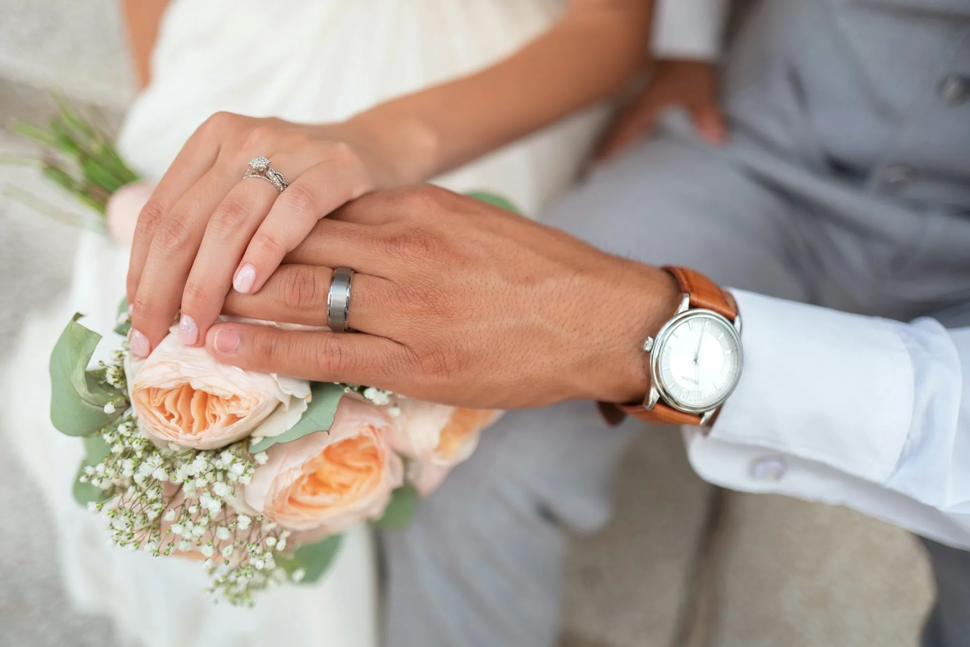 Manos de los novios con anillos sobre un ramo de flores