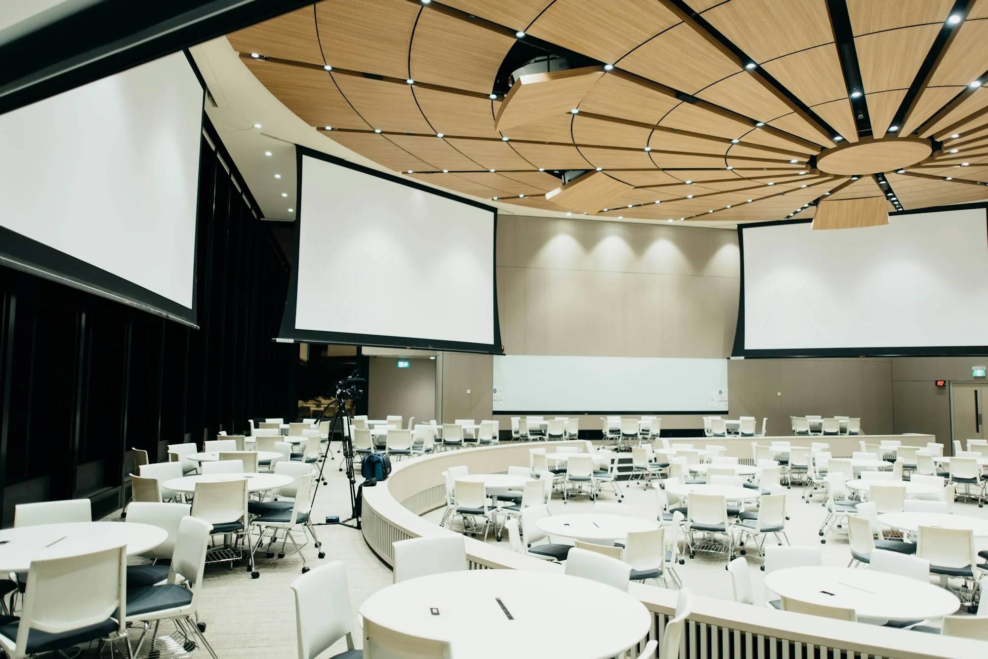 Salón de convenciones con pantallas y mesas redondas montadas